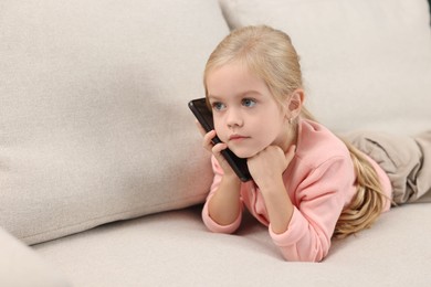 Cute little girl talking on smartphone at home, space for text