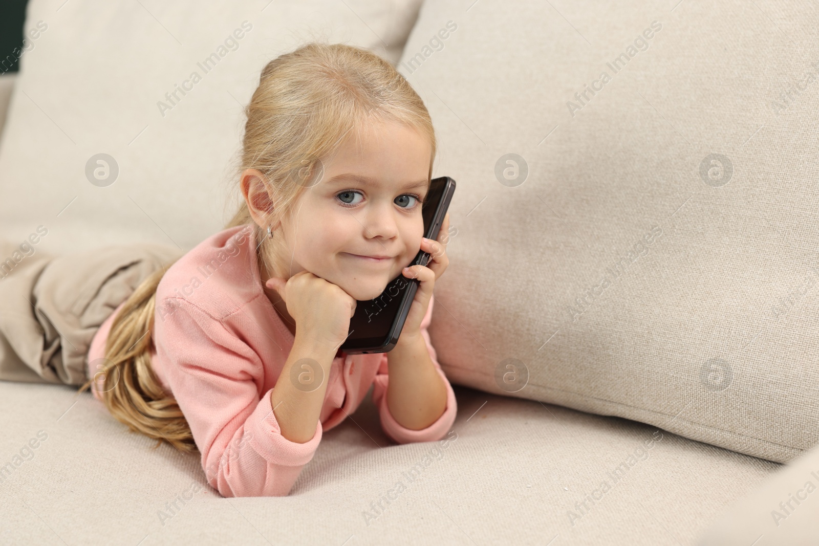 Photo of Cute little girl talking on smartphone at home, space for text