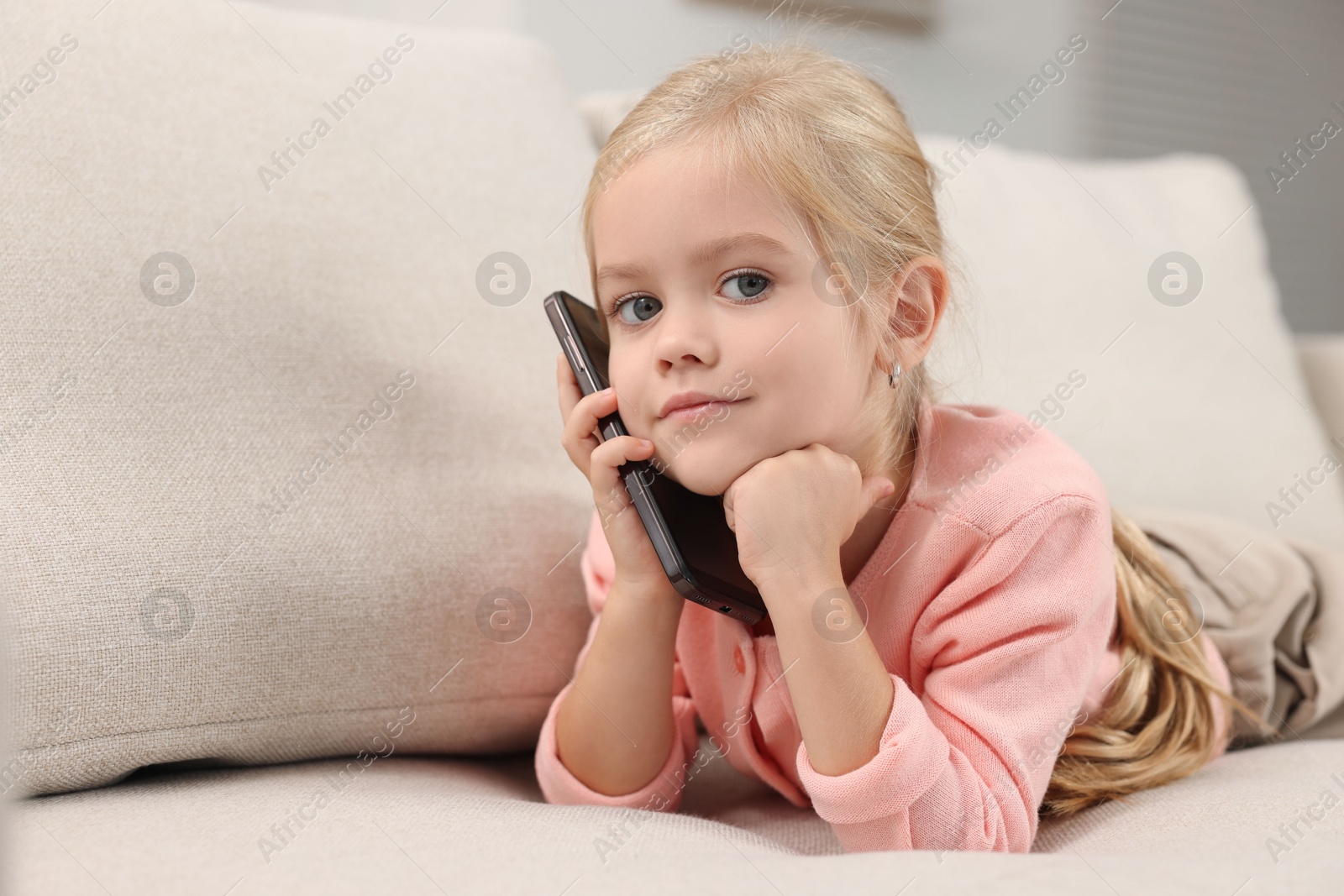 Photo of Cute little girl talking on smartphone at home, space for text