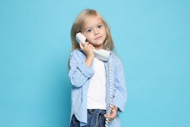 Photo of Cute little girl with handset of telephone on light blue background