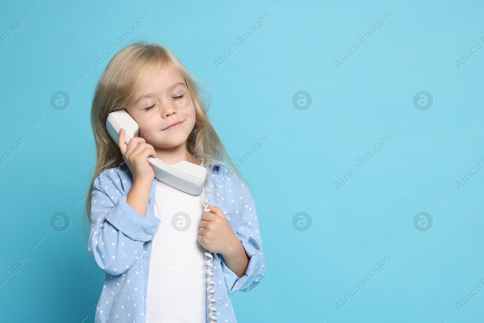 Photo of Cute little girl with handset of telephone on light blue background, space for text