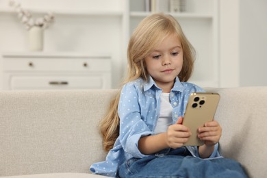 Photo of Cute little girl using smartphone on sofa at home