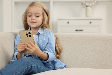 Photo of Cute little girl using smartphone on sofa at home