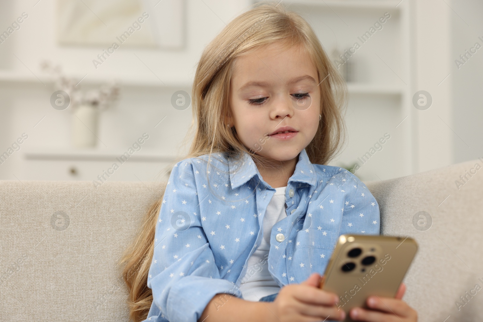 Photo of Cute little girl using smartphone on sofa at home