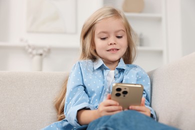 Cute little girl using smartphone on sofa at home