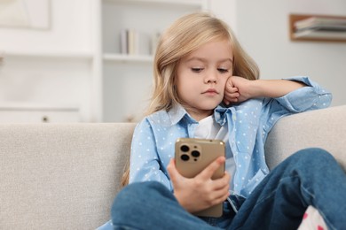 Photo of Cute little girl using smartphone on sofa at home