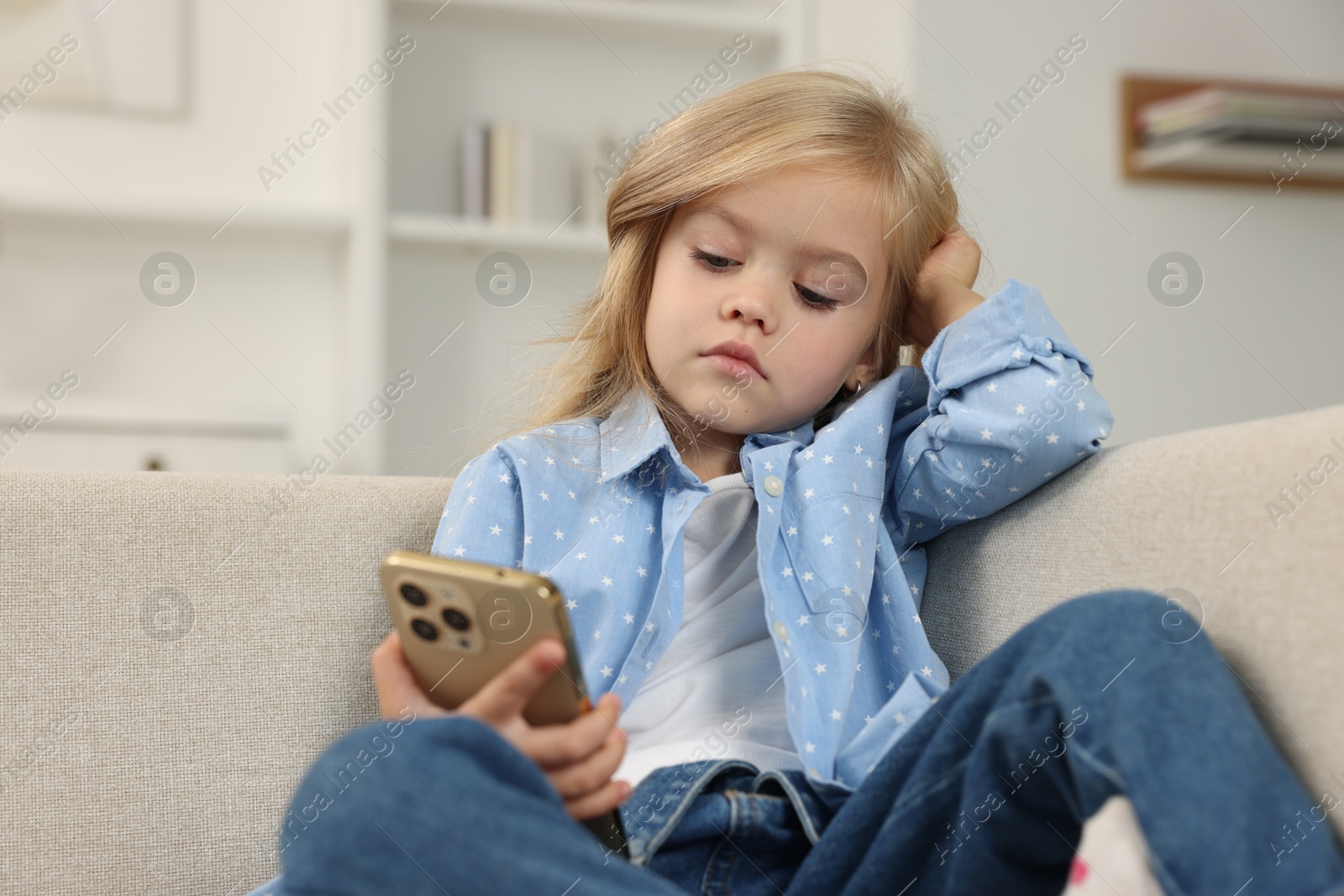 Photo of Cute little girl using smartphone on sofa at home