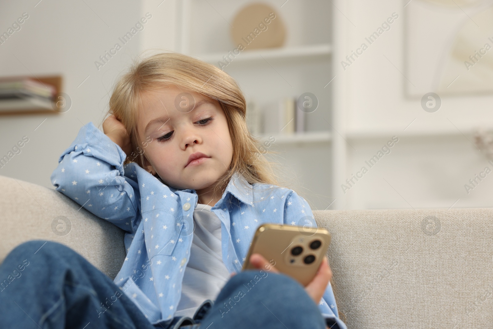 Photo of Cute little girl using smartphone on sofa at home