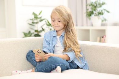 Photo of Cute little girl using smartphone on sofa at home