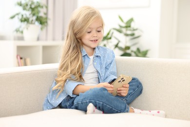 Cute little girl using smartphone on sofa at home