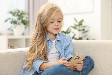 Photo of Cute little girl using smartphone on sofa at home