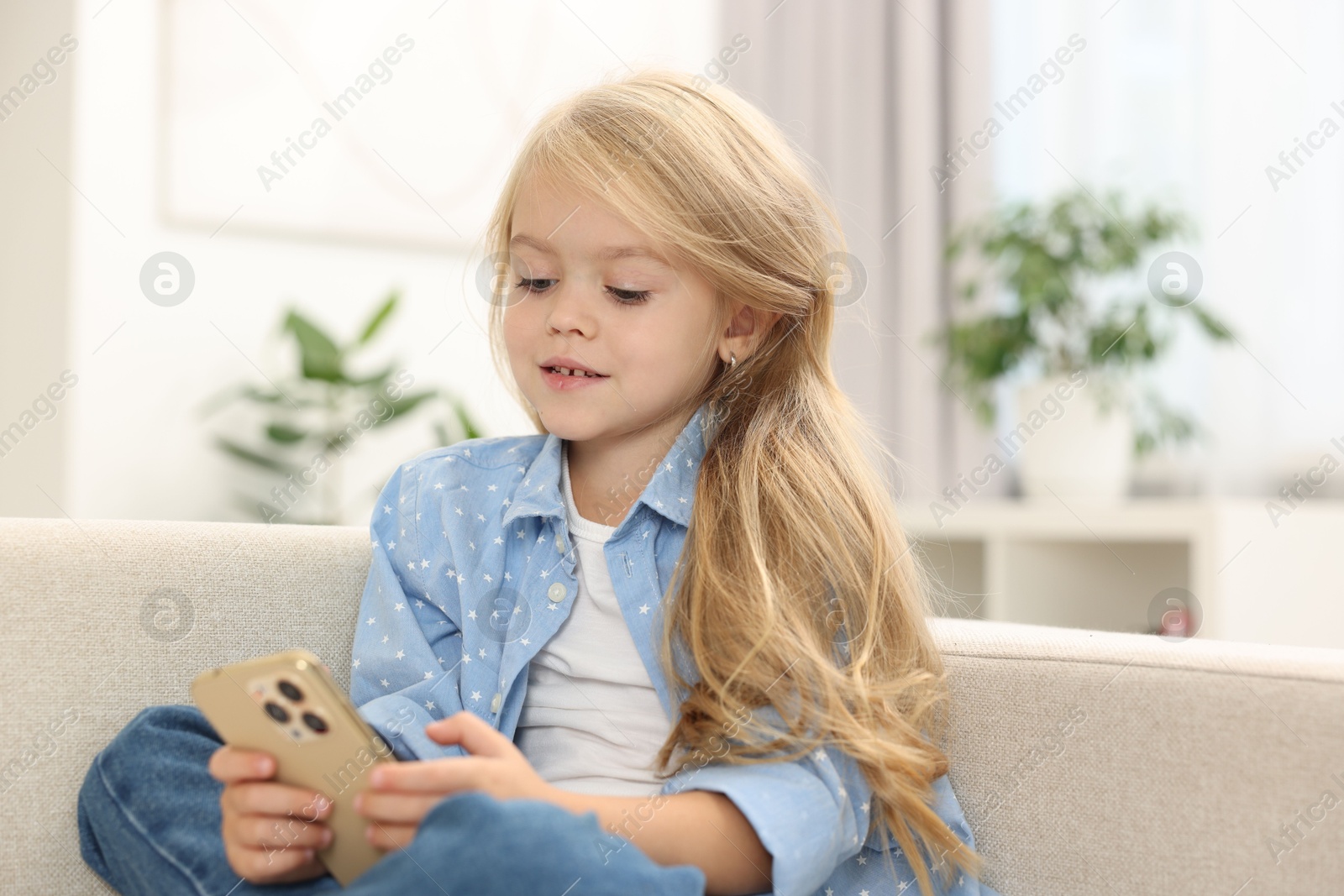 Photo of Cute little girl using smartphone on sofa at home