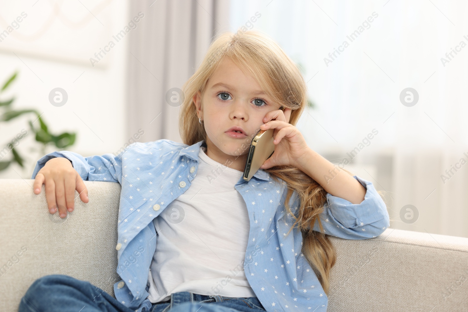 Photo of Cute little girl talking on smartphone at home