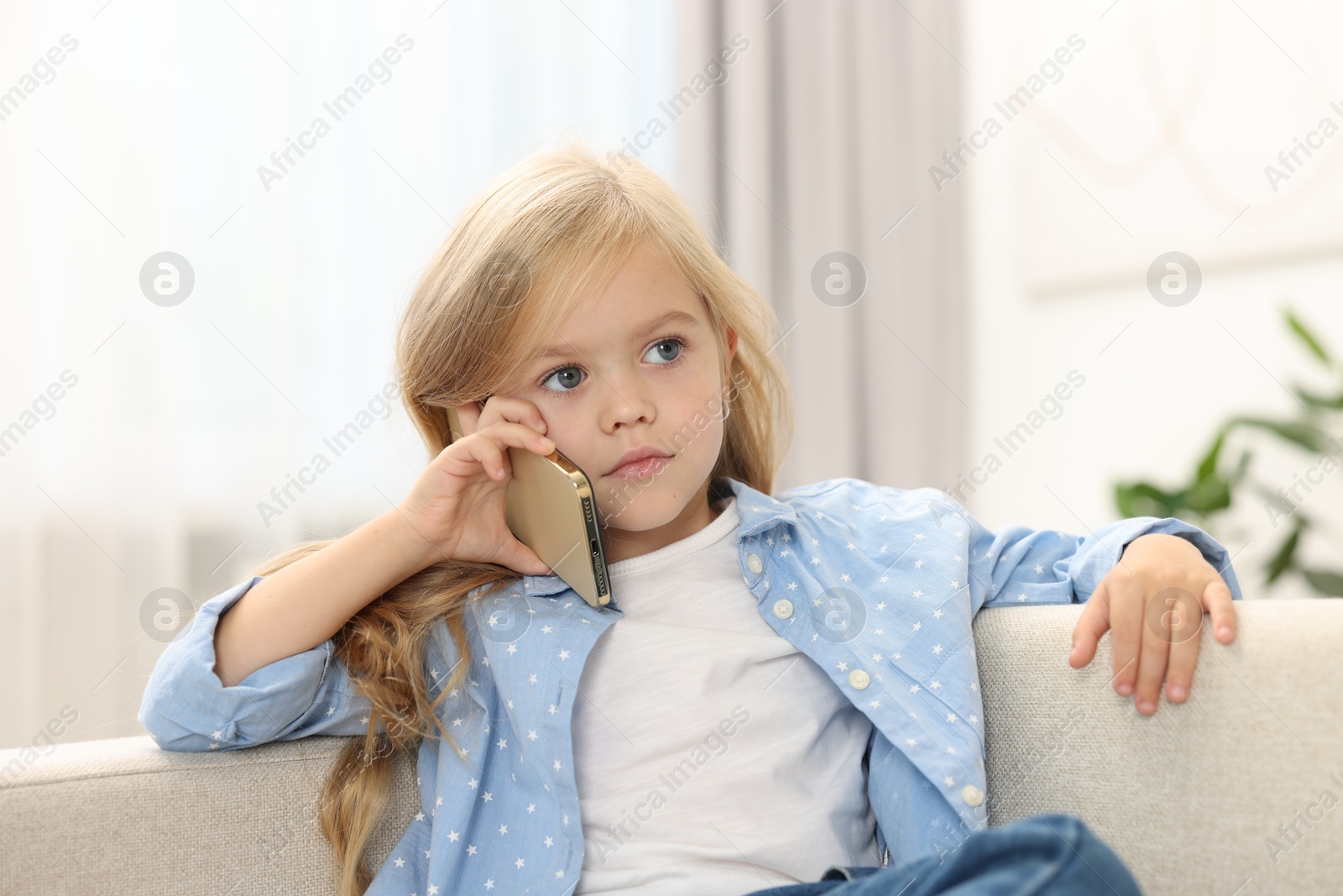 Photo of Cute little girl talking on smartphone at home