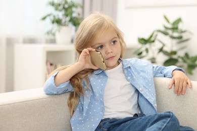 Photo of Cute little girl talking on smartphone at home