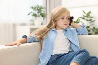 Photo of Cute little girl talking on smartphone at home