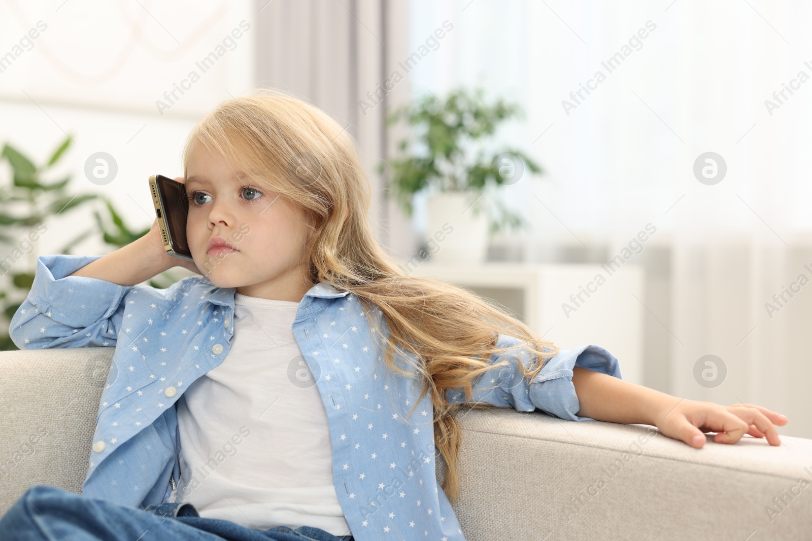 Photo of Cute little girl talking on smartphone at home