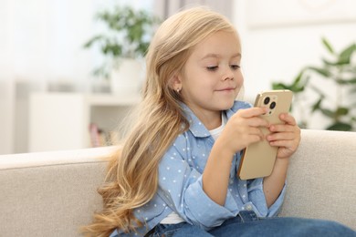 Photo of Cute little girl using smartphone on sofa at home