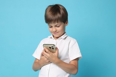 Cute little boy with smartphone on light blue background