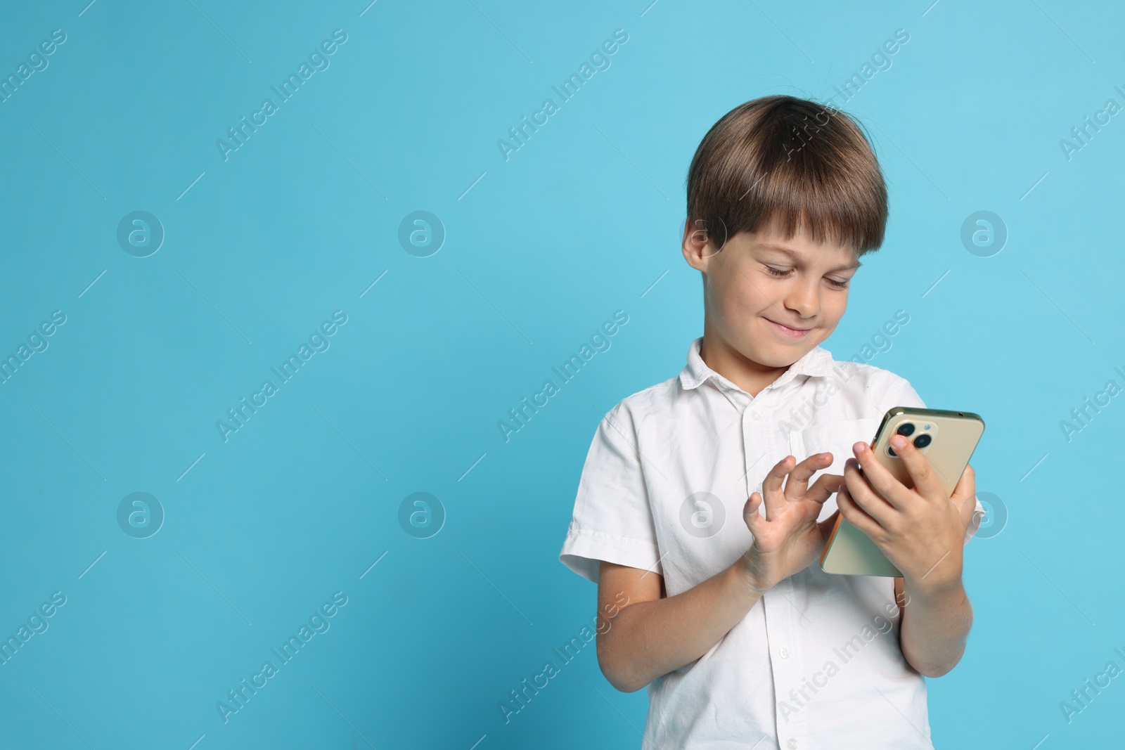 Photo of Cute little boy with smartphone on light blue background, space for text