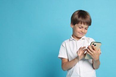 Cute little boy with smartphone on light blue background, space for text