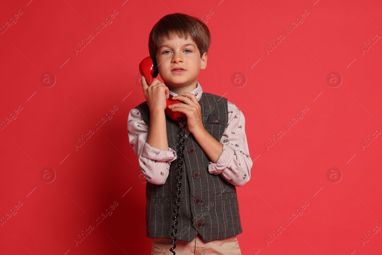 Photo of Cute little boy with handset of telephone on red background