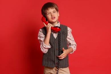 Cute little boy with handset of telephone on red background