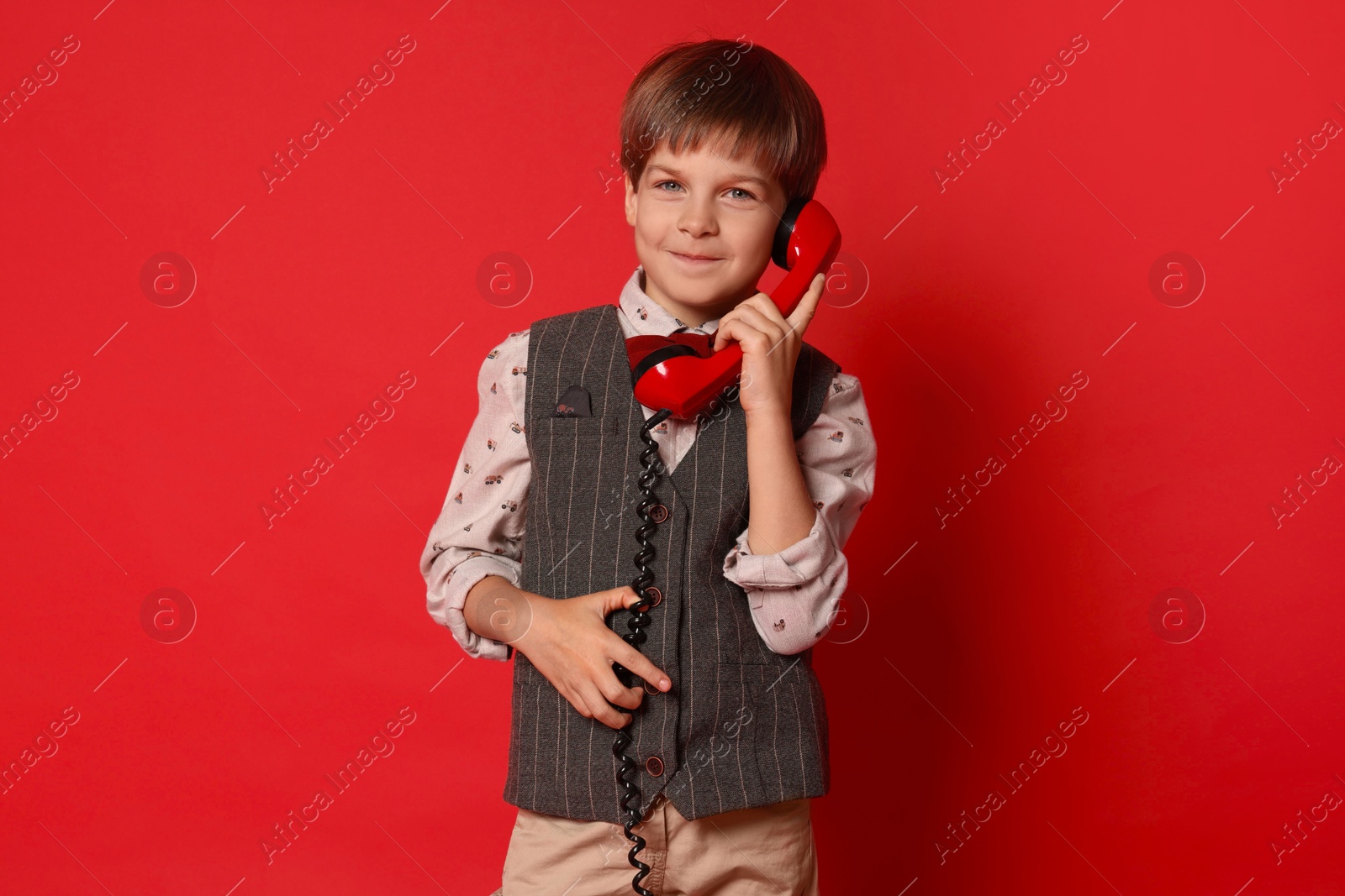 Photo of Cute little boy with handset of telephone on red background