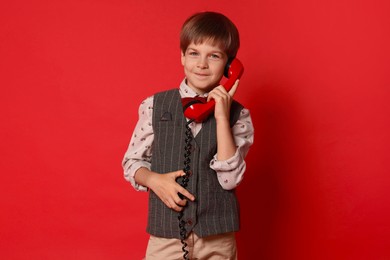 Cute little boy with handset of telephone on red background