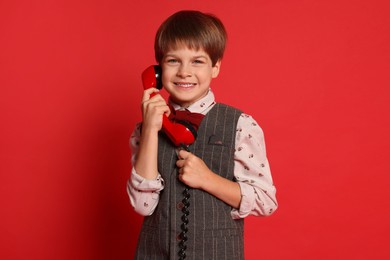 Photo of Cute little boy with handset of telephone on red background