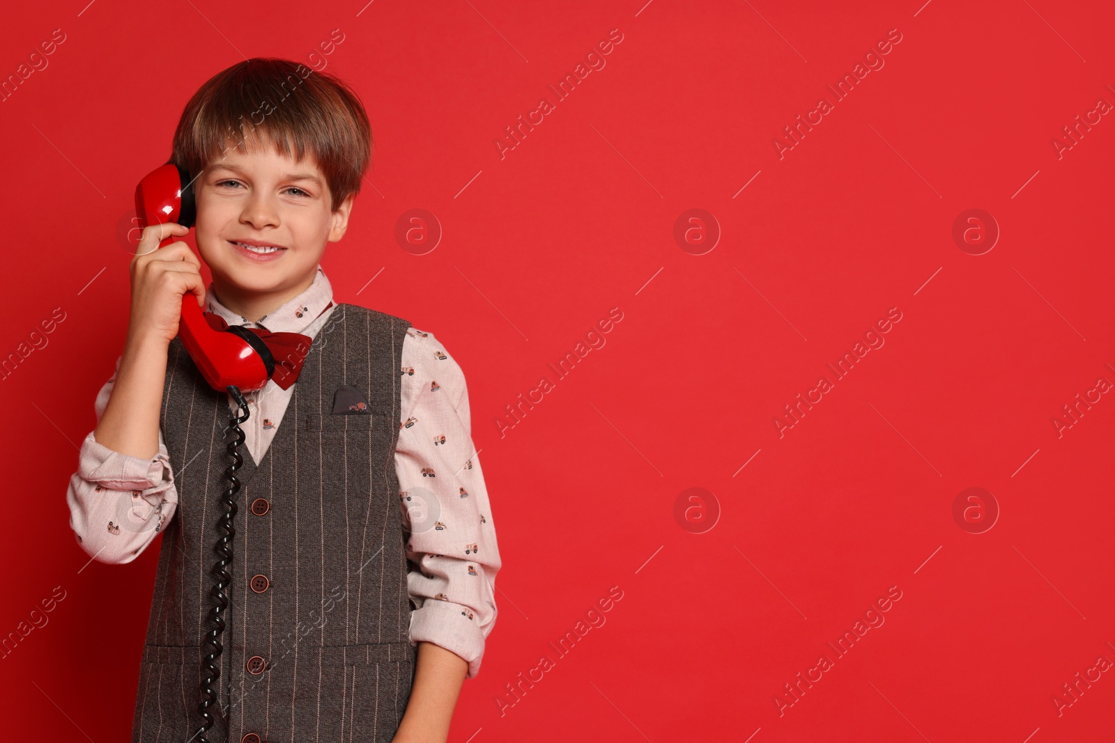 Photo of Cute little boy with handset of telephone on red background, space for text