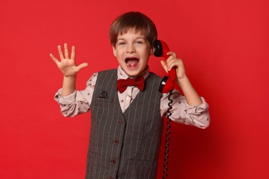 Photo of Cute little boy with handset of telephone on red background