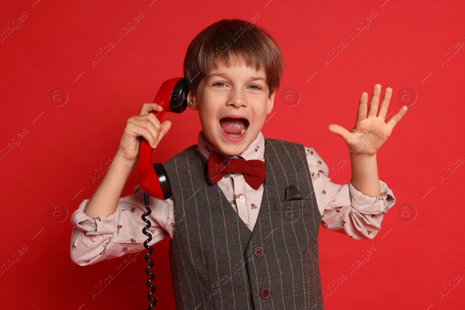 Photo of Cute little boy with handset of telephone on red background