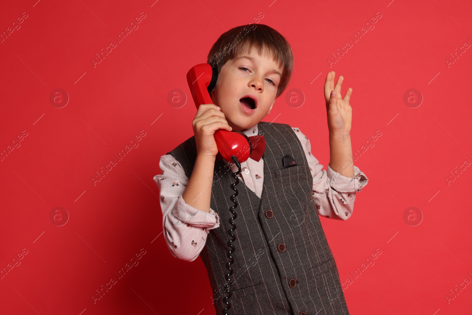 Photo of Cute little boy with handset of telephone on red background