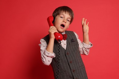 Cute little boy with handset of telephone on red background