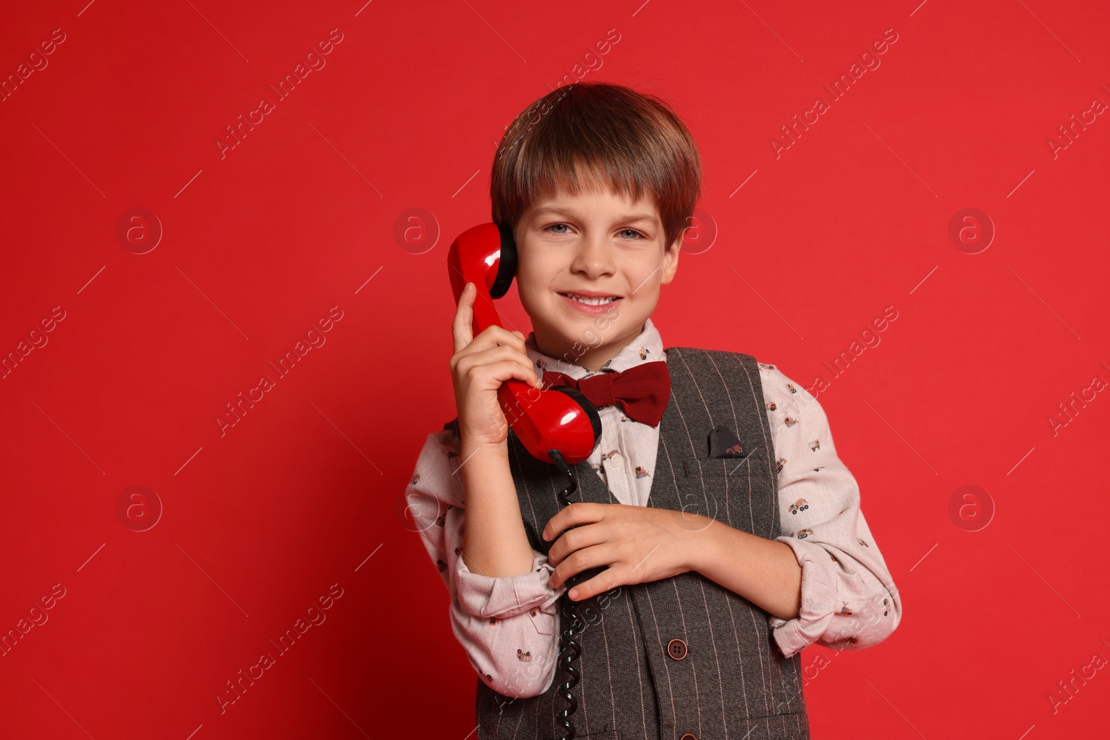 Photo of Cute little boy with handset of telephone on red background, space for text