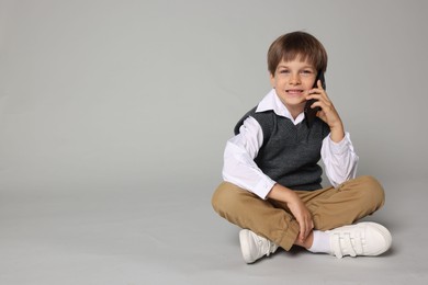 Photo of Cute little boy talking on smartphone against grey background, space for text