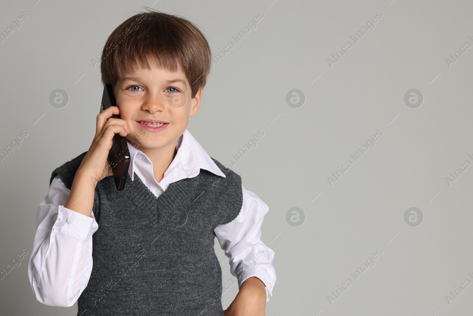 Photo of Cute little boy talking on smartphone against grey background, space for text