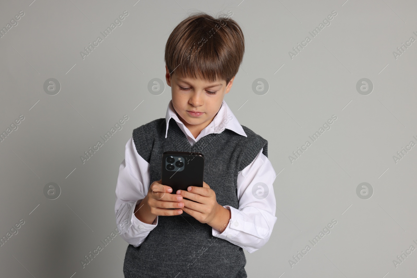 Photo of Cute little boy with smartphone on grey background