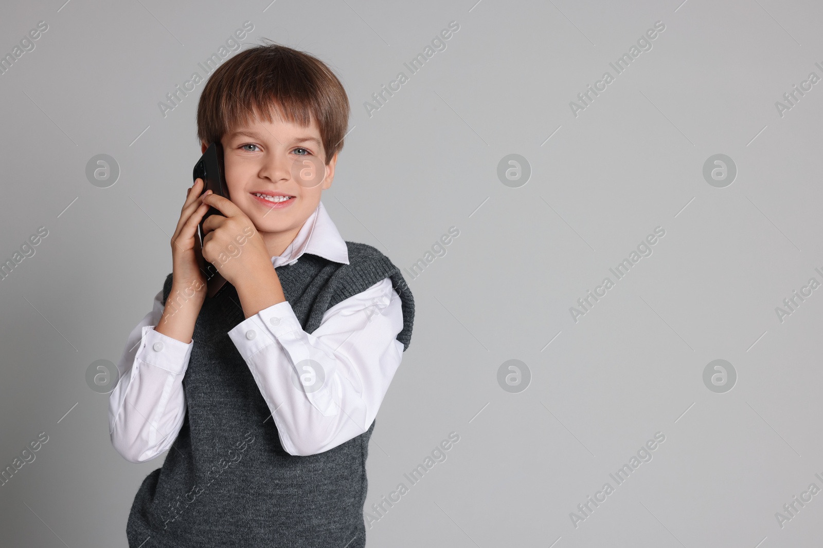 Photo of Cute little boy talking on smartphone against grey background, space for text