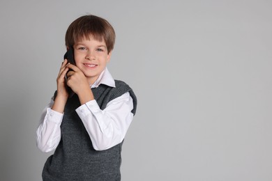 Cute little boy talking on smartphone against grey background, space for text