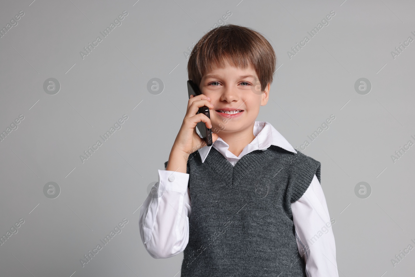 Photo of Cute little boy talking on smartphone against grey background, space for text