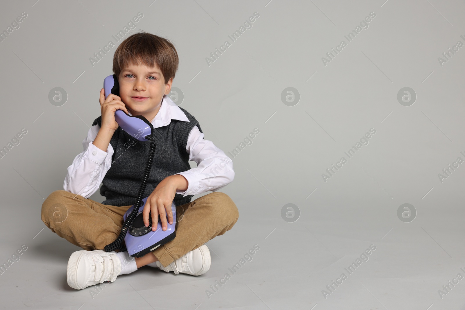 Photo of Cute little boy with old telephone on grey background, space for text