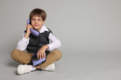 Cute little boy with old telephone on grey background, space for text