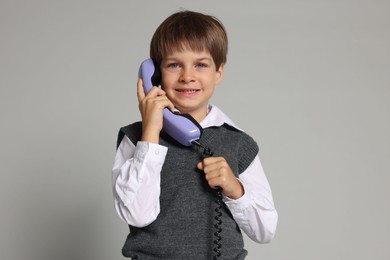 Photo of Cute little boy with handset of telephone on grey background