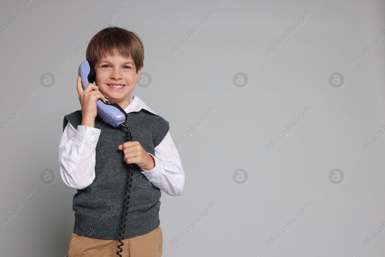 Photo of Cute little boy with handset of telephone on grey background, space for text