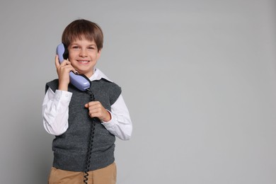 Cute little boy with handset of telephone on grey background, space for text