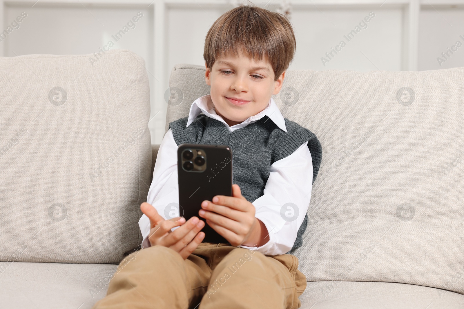 Photo of Cute little boy using smartphone on sofa at home