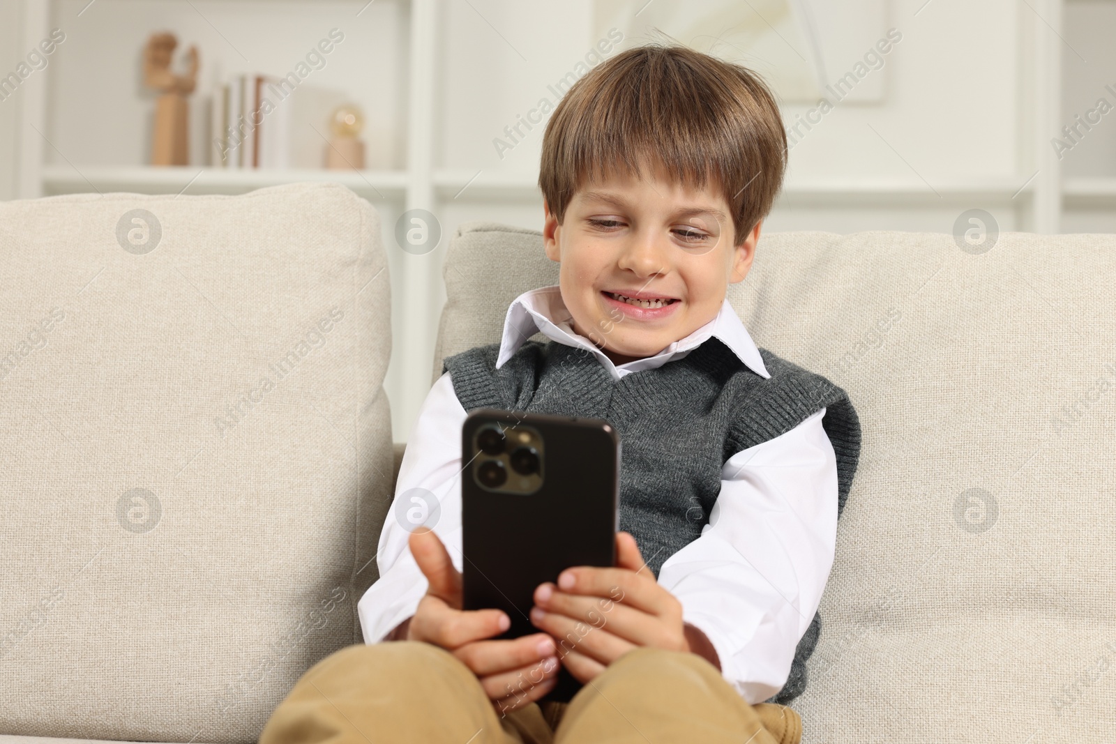 Photo of Cute little boy using smartphone on sofa at home