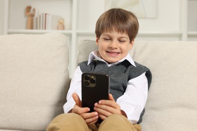 Cute little boy using smartphone on sofa at home